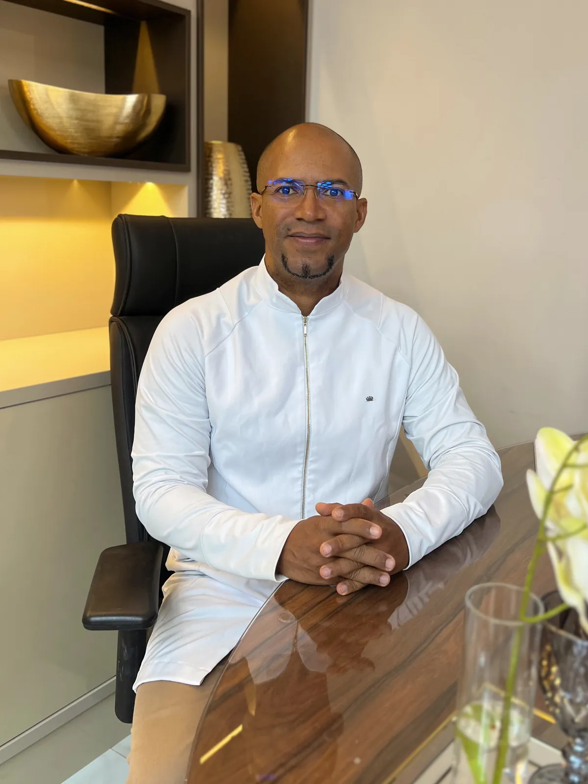 Dr. Lester Otomuro de jaleco branco, sentado à mesa do consultório, com as mãos entrelaçadas